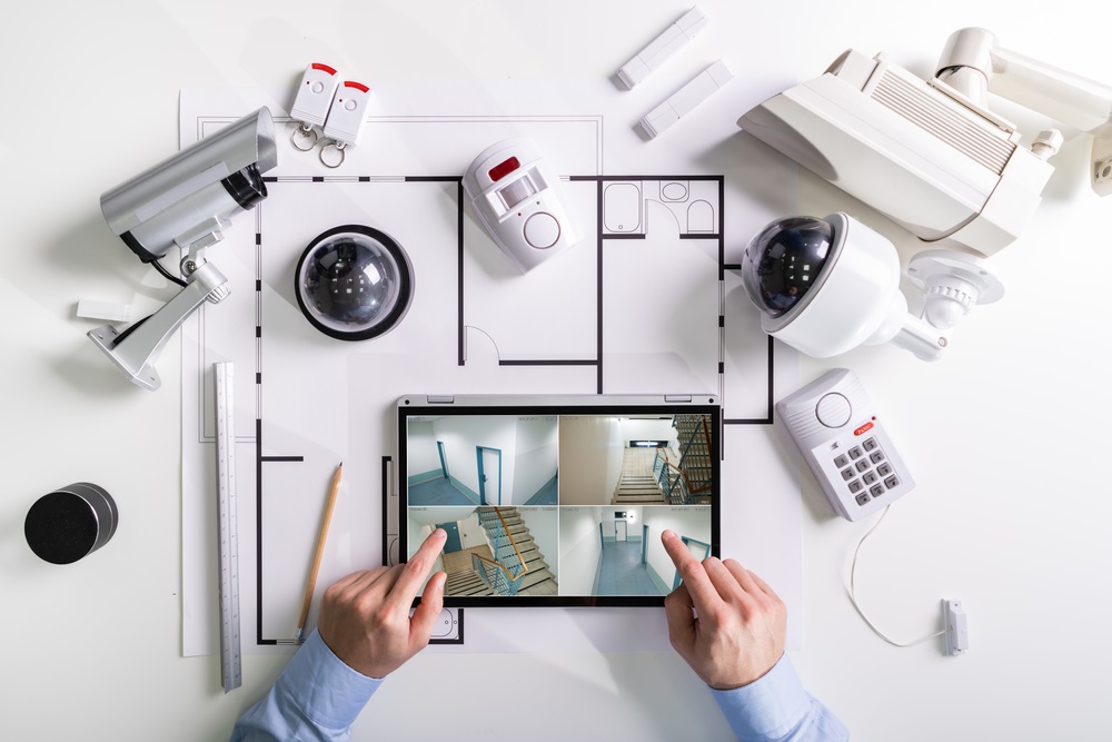 Close-up Of A Person Watching Footage On Digital Tablet With Security Equipment On Blueprint