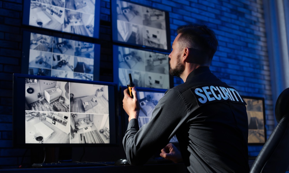Male security guard with portable transmitter monitoring modern CCTV cameras indoors