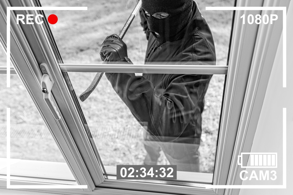 CCTV view of burglar breaking in to home through window with crowbar